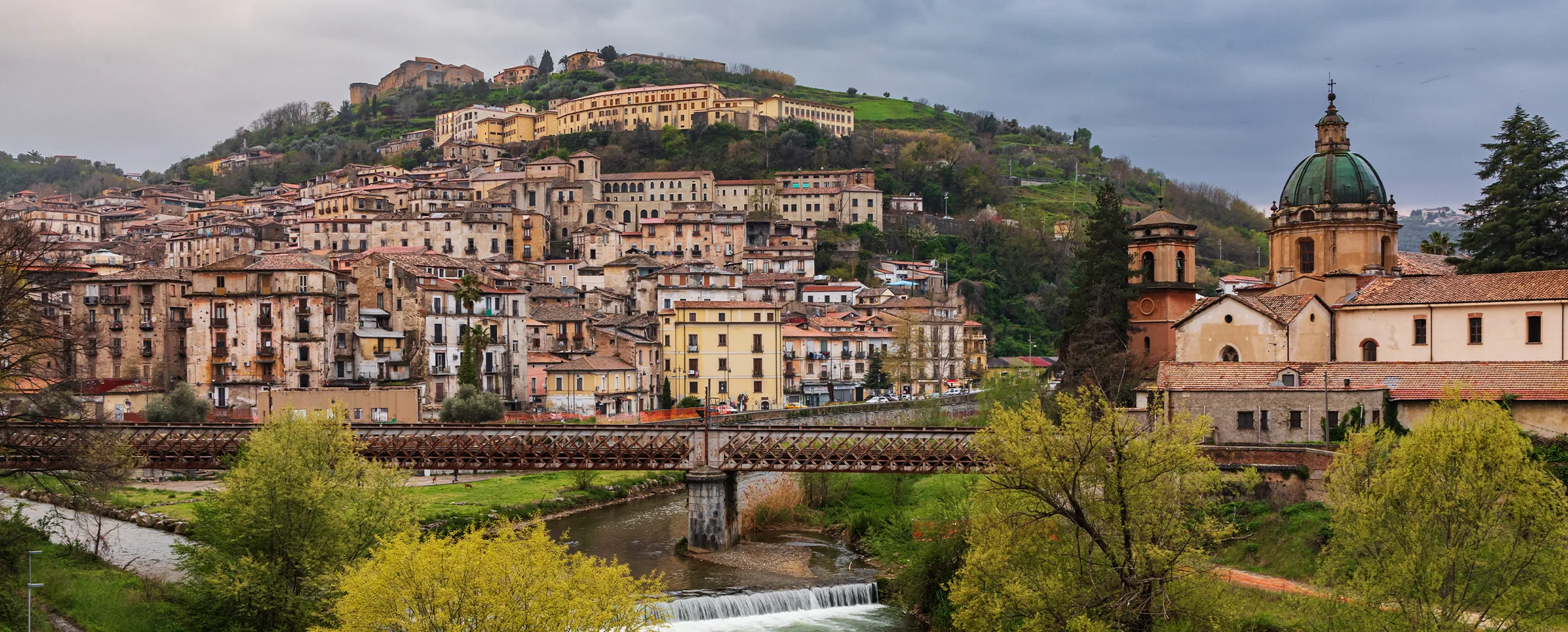 Cosenza's old town on its hill, with the Castle at the top, an iron bridge over the river and the dome of a church on the right